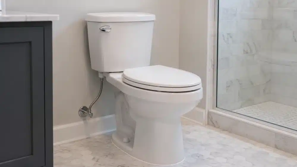 Newly installed white toilet with connected supply line bolt caps and clean caulking on a spotless tiled bathroom floor toilet installation